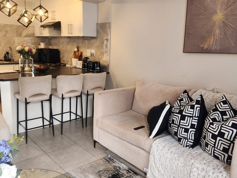 Modern open-plan living area featuring a well-appointed kitchen with stone countertops, breakfast bar, and contemporary pendant lighting, seamlessly integrated with the lounge space.