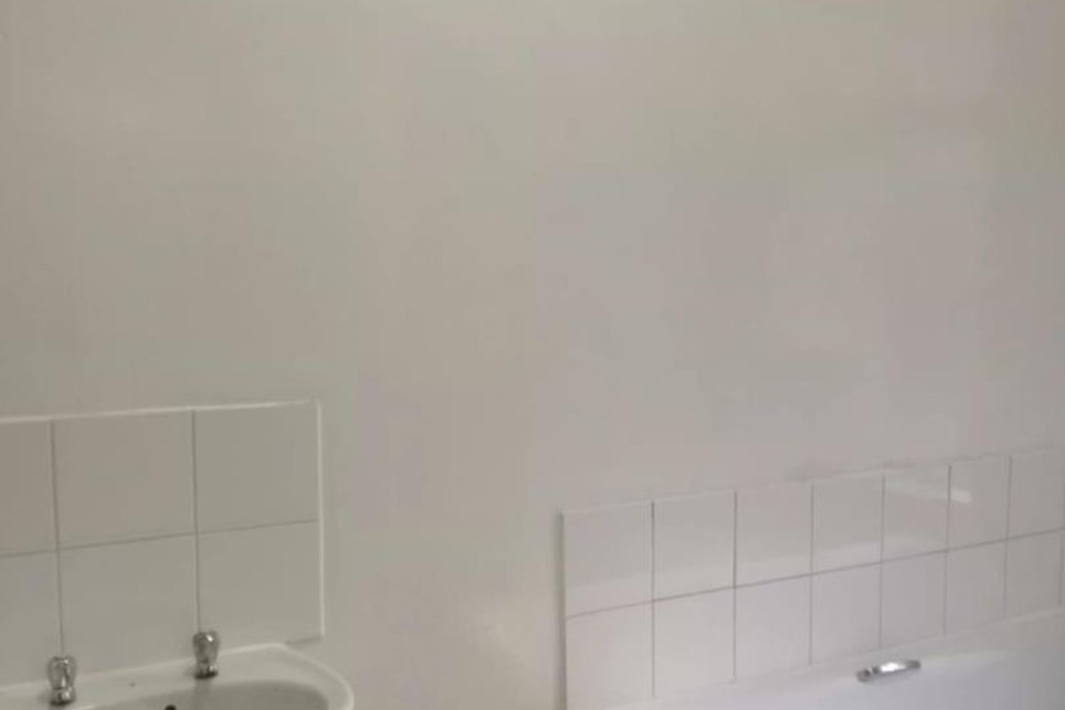 A basic, empty bathroom featuring a white pedestal washbasin and a built-in bathtub with white ceramic wall tiling.