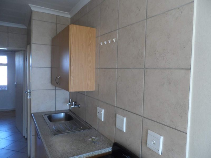 A functional laundry area featuring a stainless steel sink, tiled splashback, and wall-mounted cabinetry, providing essential utility space.