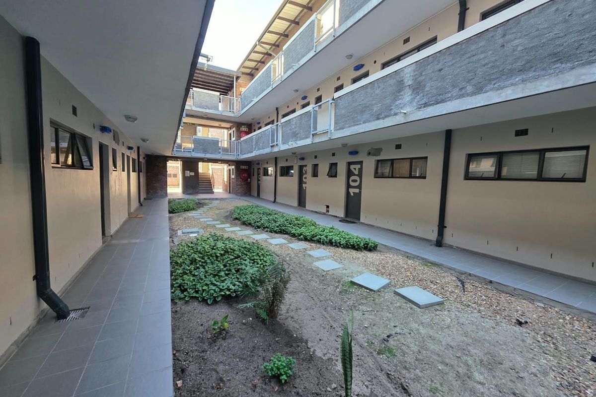 A view of the apartment complex courtyard featuring tiled walkways, metal railings, and a landscaped garden area between building wings.