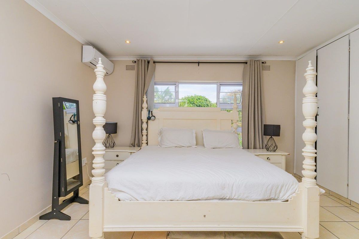 A well-lit bedroom featuring tiled flooring, built-in cupboards, and a wall-mounted air conditioning unit.