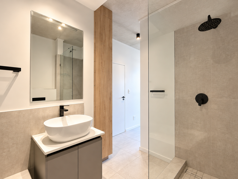 Modern bathroom featuring a vessel sink vanity, walk-in shower with glass screen, and contemporary black matte fixtures with neutral tiled finishes.
