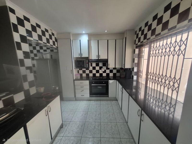 Functional kitchen featuring built-in cabinetry, granite countertops, integrated oven, hob, and extractor fan, finished with distinctive checkered wall tiling.