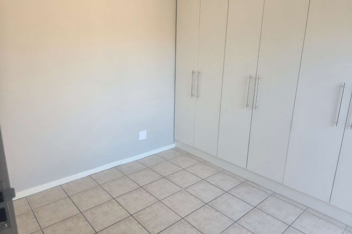 A clean, empty bedroom featuring neutral tiled flooring and modern, floor-to-ceiling built-in cupboards with sleek handles.