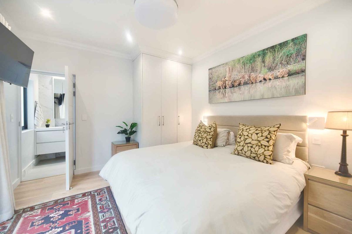 A well-maintained bedroom featuring built-in cupboards, laminate flooring, recessed lighting, and an adjoining en-suite bathroom.