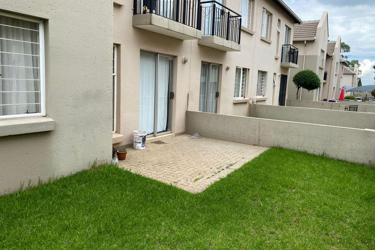 Rear view of the apartment complex featuring a paved patio area, small private lawn, and sliding door access to the ground floor unit.