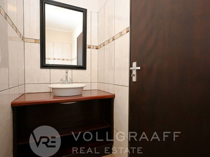 A compact bathroom featuring a vessel sink on a wooden vanity cabinet, complemented by neutral wall tiling and a framed mirror.