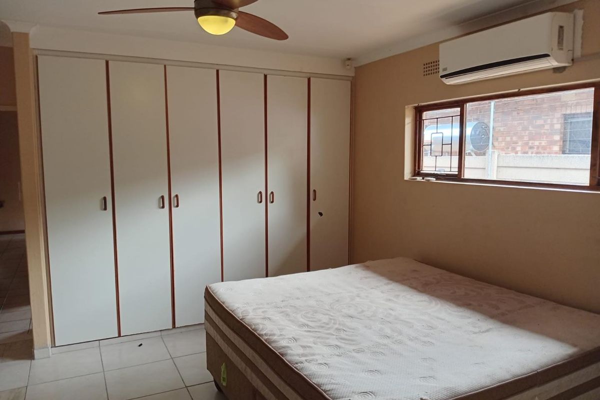 A bedroom featuring built-in cupboards, a ceiling fan, and a wall-mounted air conditioning unit, finished with tiled flooring.