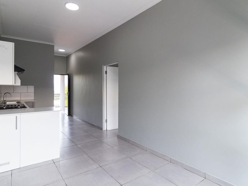 An open-plan living and kitchen area featuring modern grey walls, neutral tiled flooring, and a compact kitchen with built-in cabinetry and gas hob.