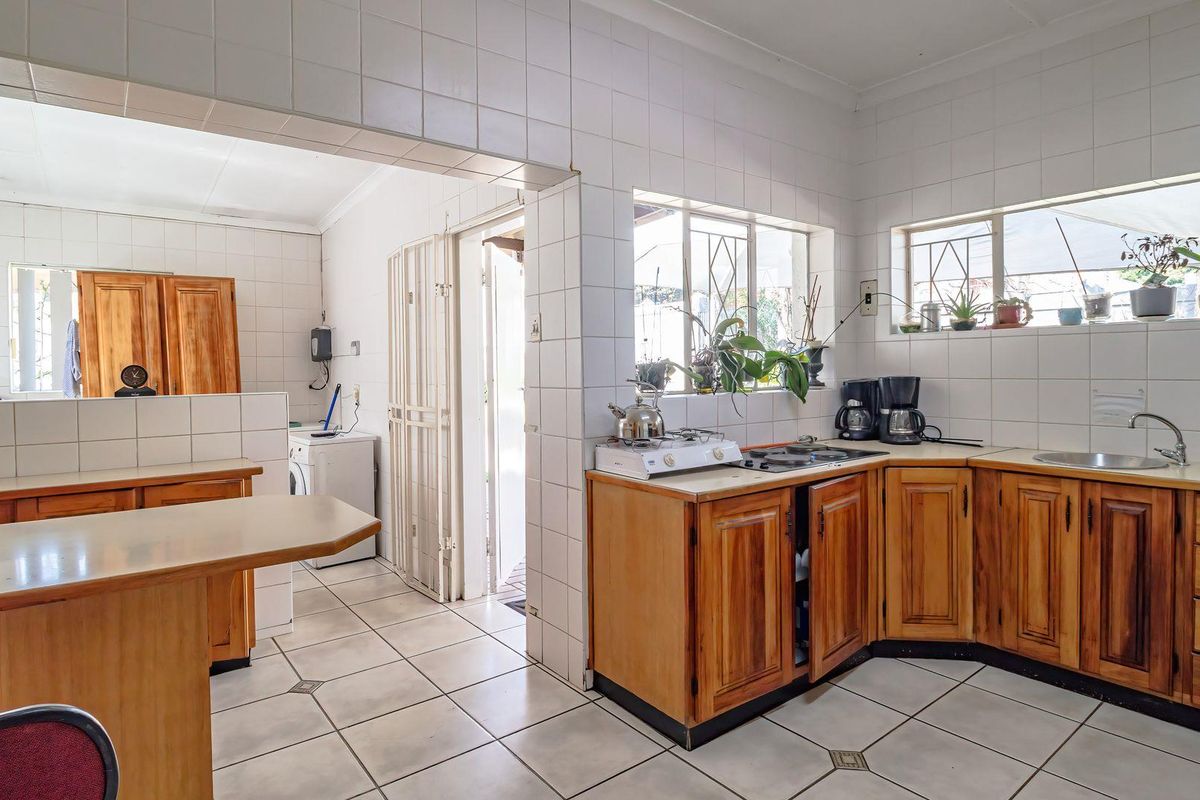 A functional kitchen featuring wooden cabinetry, tiled flooring, and a tiled splashback, with an adjacent utility area and direct access to the exterior.