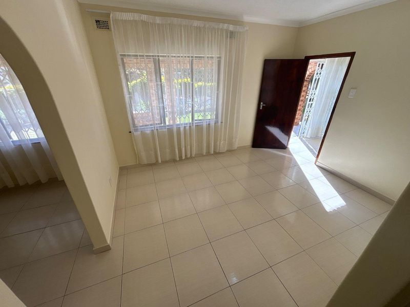 A bright, empty living room featuring neutral tiled flooring, an arched entryway, and direct access to an outdoor patio area.