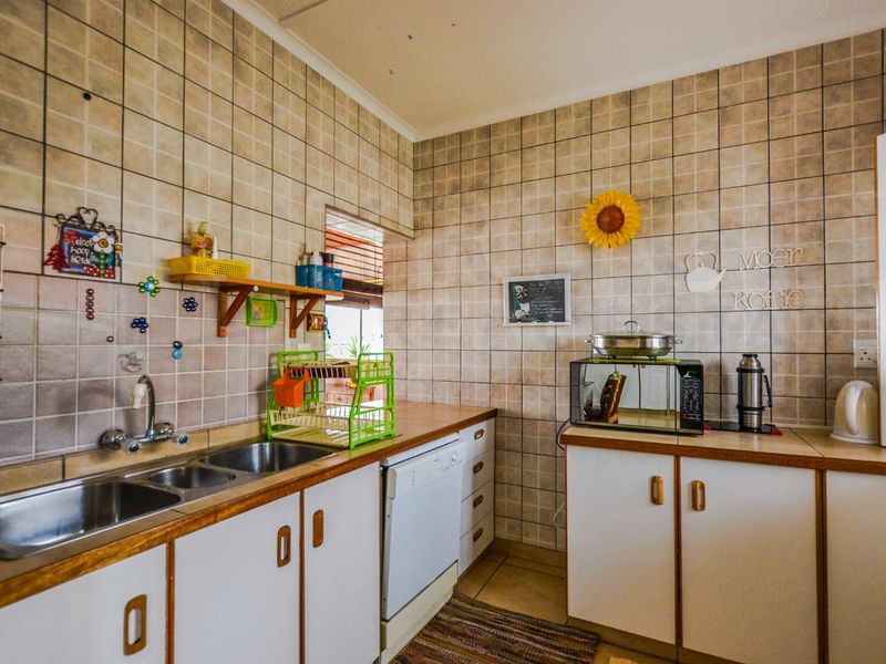 A functional kitchen featuring a double stainless steel sink, tiled splashback, and ample built-in cabinetry with laminate countertops.