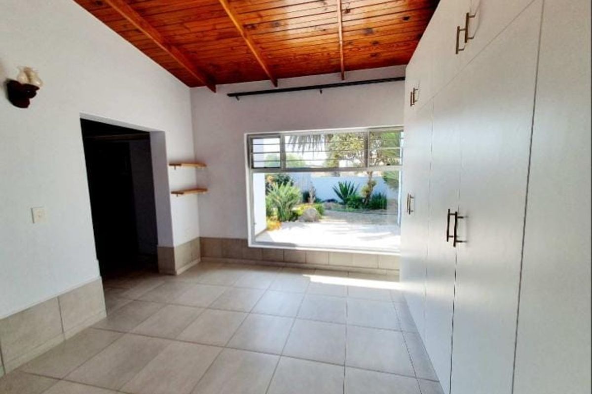 A bright, empty room featuring a high timber-paneled ceiling, large window with garden view, and extensive built-in storage cabinetry.