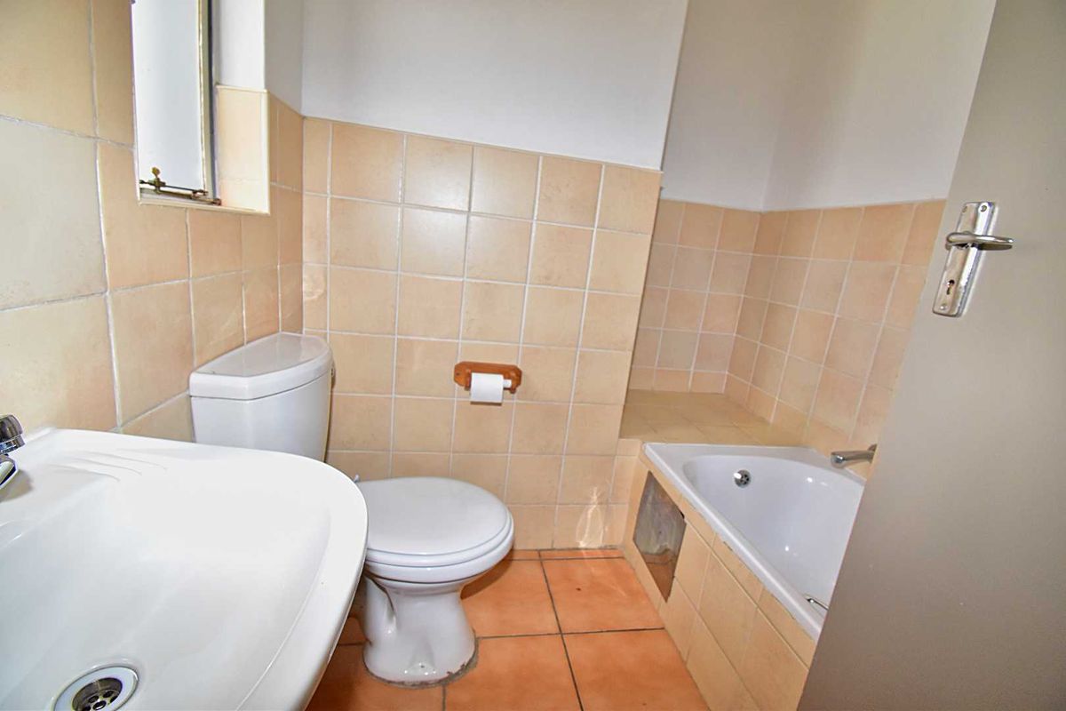 A functional bathroom featuring a built-in bathtub, standard toilet, and pedestal basin with neutral wall tiling and terracotta-style floor tiles.