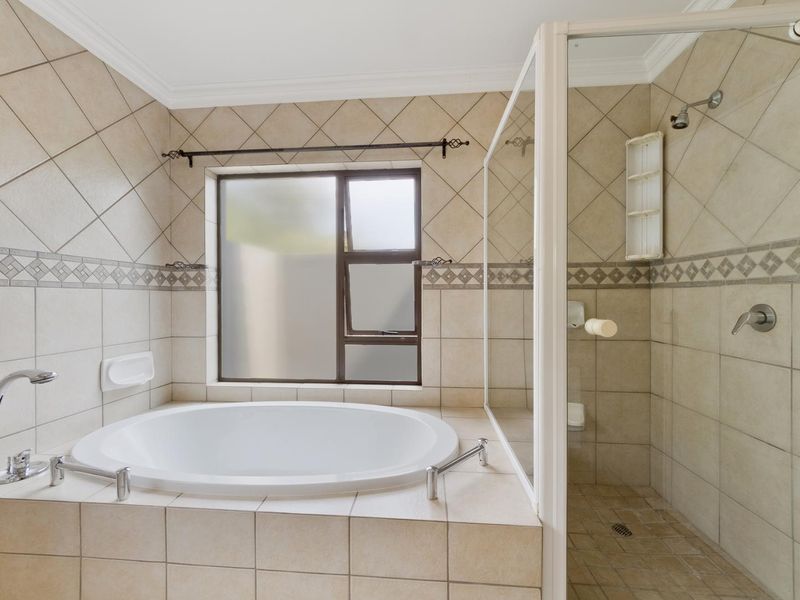 A functional bathroom featuring a built-in circular bathtub, a separate shower enclosure with glass screen, and neutral tiled finishes throughout.