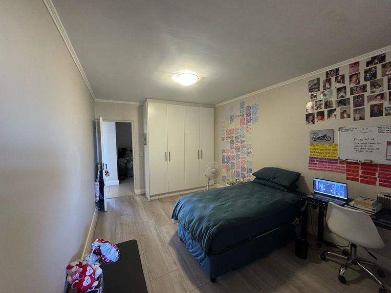 A functional bedroom featuring light-toned laminate flooring, a built-in wardrobe with white cabinetry, and a flush mount ceiling light.