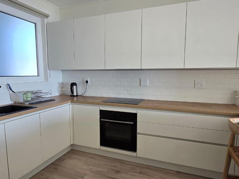 Modern kitchen featuring white cabinetry, wood-look countertops, subway tile backsplash, and integrated appliances including an oven and hob.