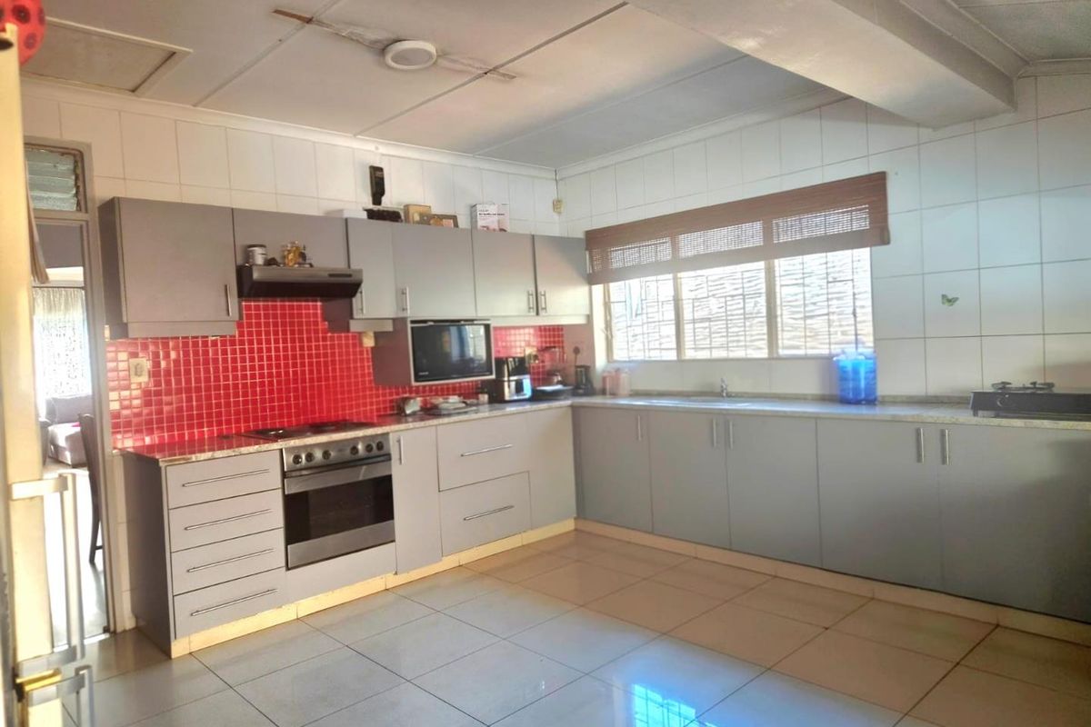 Functional kitchen featuring grey cabinetry, a vibrant red tiled backsplash, built-in oven, extractor fan, and tiled flooring.