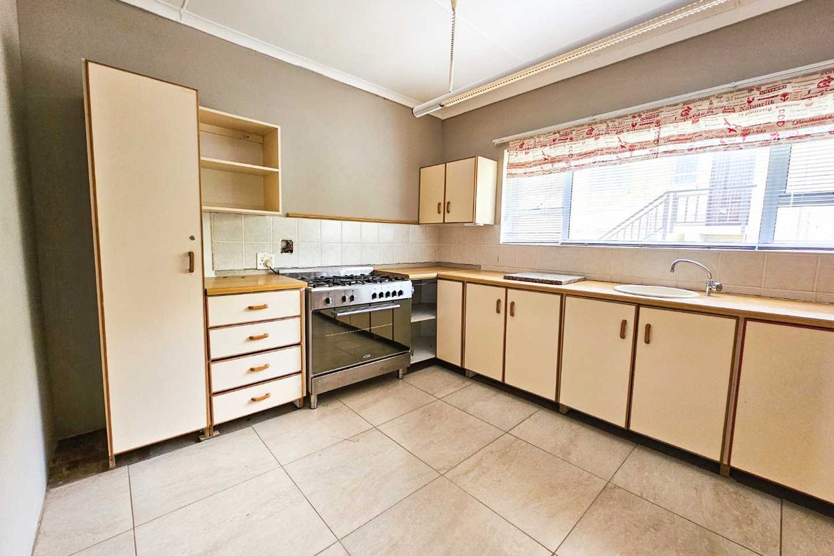 A functional kitchen featuring light-toned cabinetry, a freestanding gas stove, tiled flooring, and a single basin sink with a tiled backsplash.