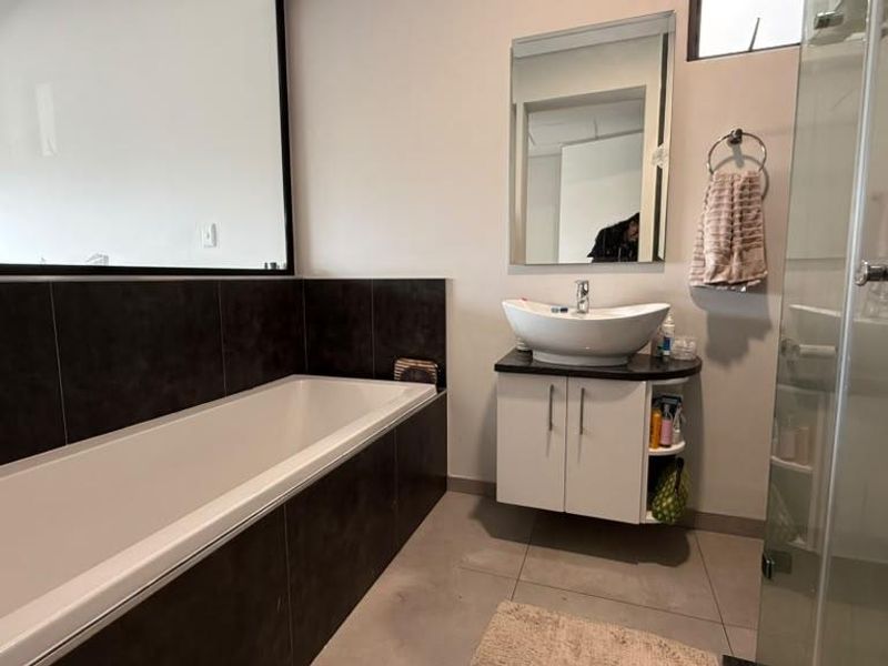 Modern bathroom featuring a built-in bathtub with dark tiling, a vessel sink vanity, and a separate glass-enclosed shower.