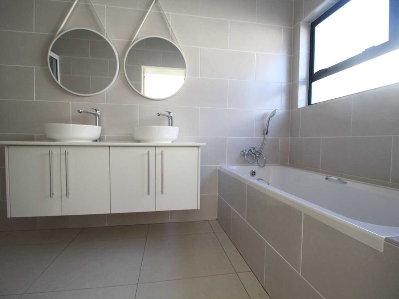 Modern bathroom featuring a double vanity with vessel sinks, wall-mounted faucets, and a tiled built-in bathtub with a handheld shower mixer.