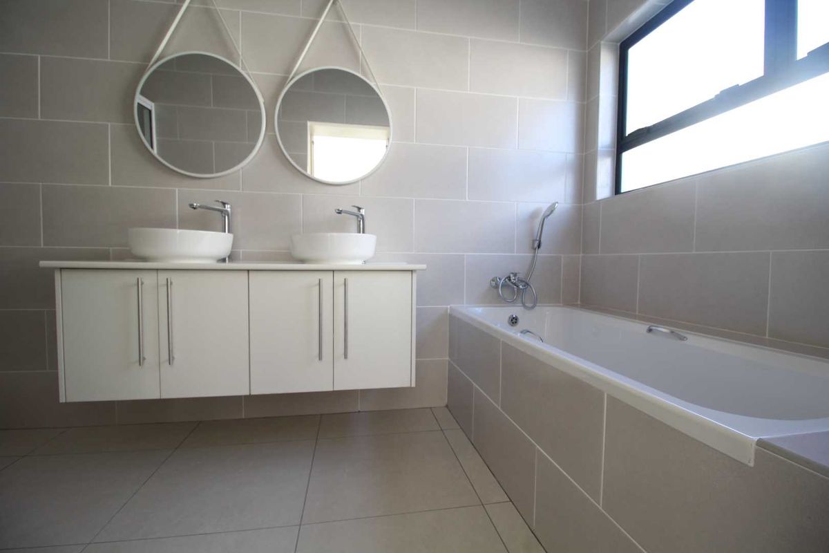 Modern bathroom featuring a double vanity with vessel sinks, wall-mounted faucets, and a tiled built-in bathtub with a handheld shower mixer.