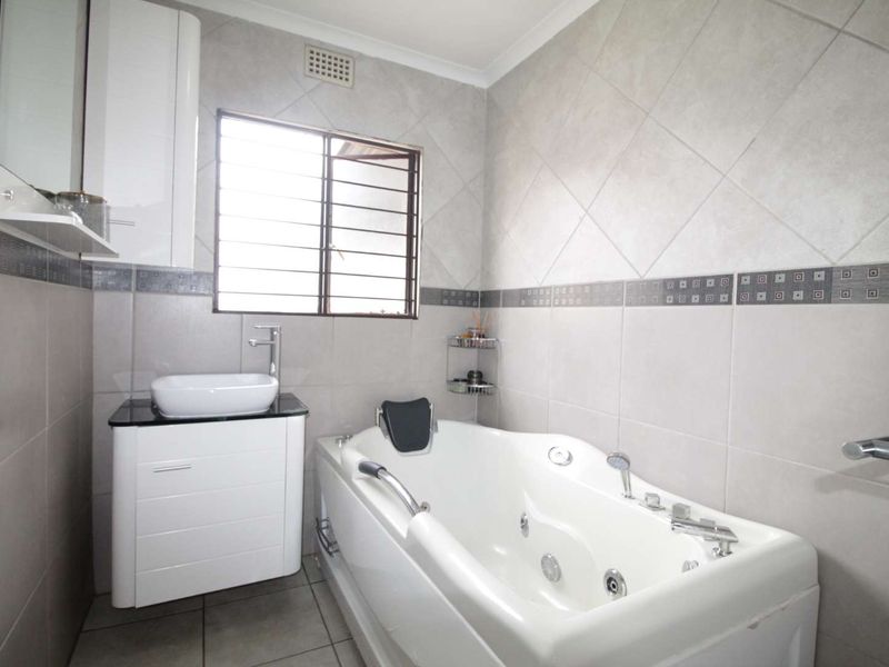 Modern bathroom featuring a large jacuzzi bathtub, a sleek vessel sink with vanity cabinet, and neutral wall tiling.