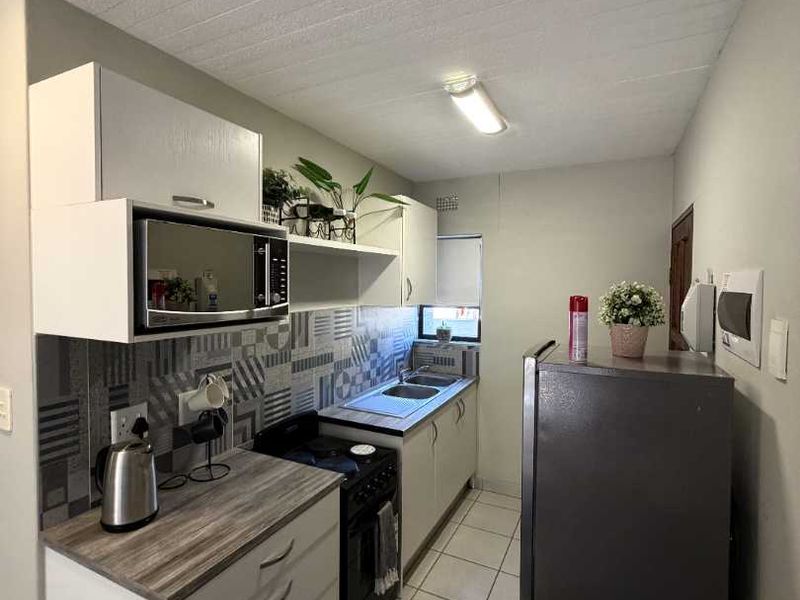 A compact, functional kitchen featuring modern grey cabinetry, patterned tiled backsplash, laminate countertops, and tiled flooring.