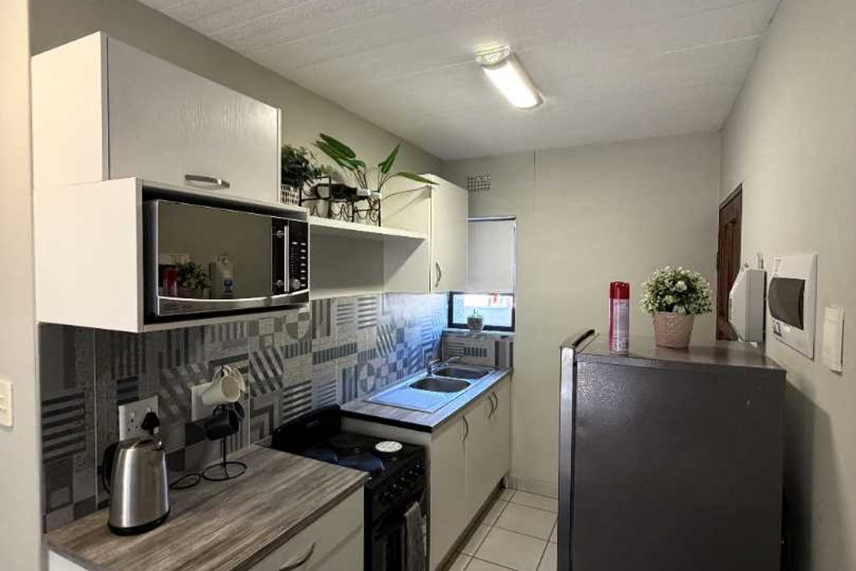 A compact, functional kitchen featuring modern grey cabinetry, patterned tiled backsplash, laminate countertops, and tiled flooring.