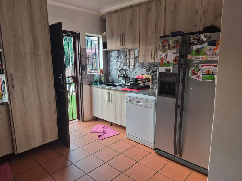 A functional kitchen featuring wood-look cabinetry, stone-effect backsplash, tiled flooring, and direct access to the exterior.