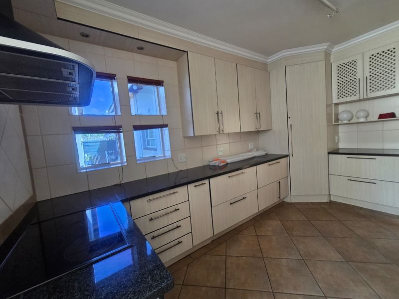 A functional kitchen featuring light-toned cabinetry, dark granite countertops, tiled backsplash, and ceramic floor tiles, offering a clean and well-maintained workspace.