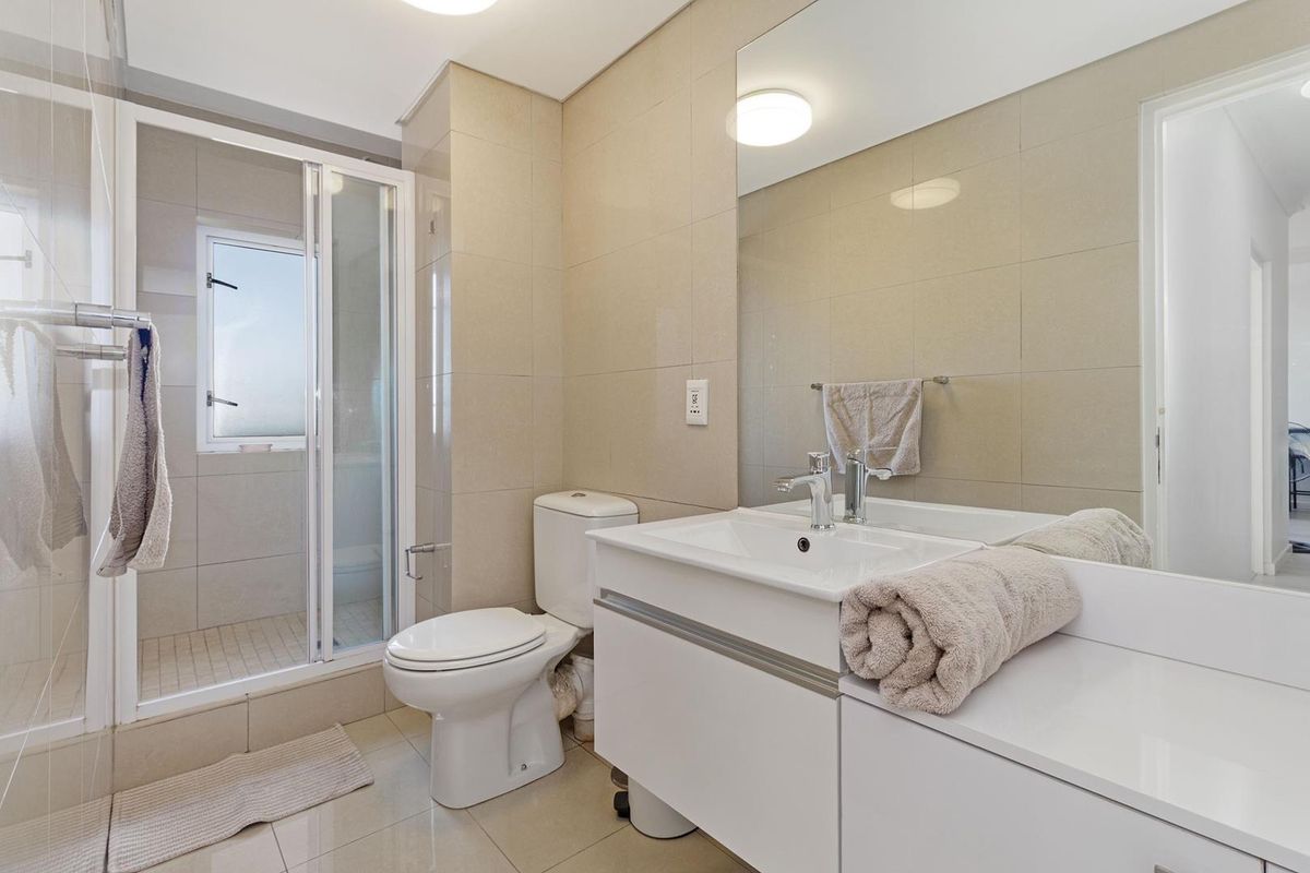 A modern, well-maintained bathroom featuring a glass-enclosed shower, a sleek white vanity with basin, and neutral wall tiling.