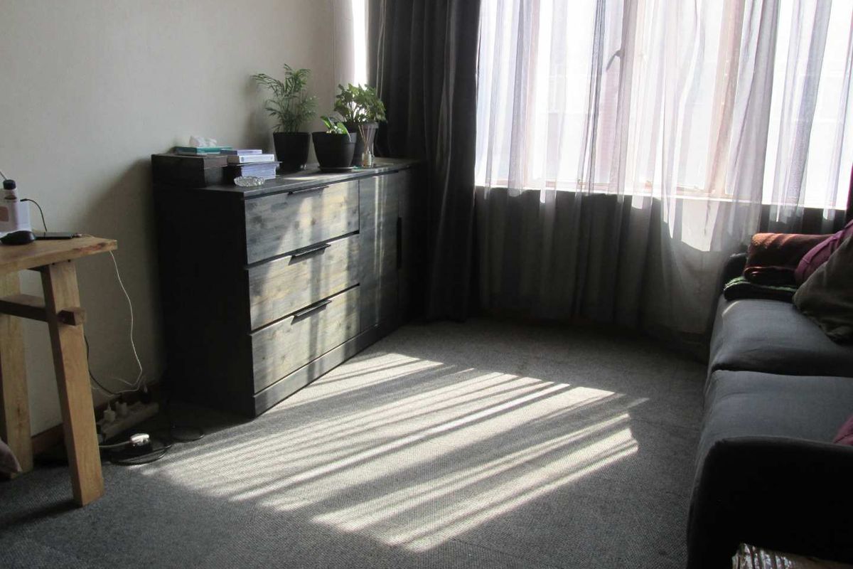 A living room area featuring wall-to-wall carpeting and large windows with curtains, providing natural light to the space.