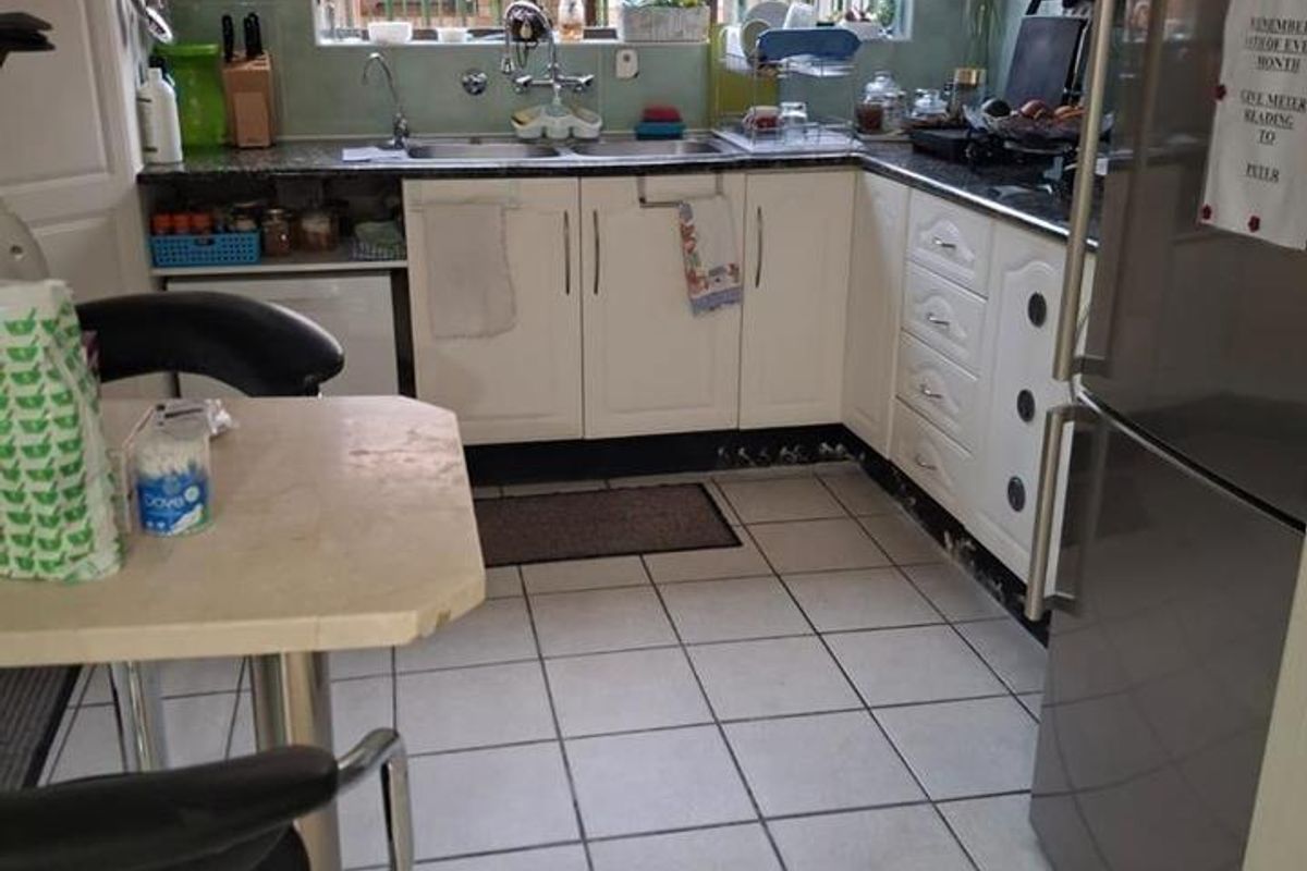 A functional kitchen featuring white cabinetry, granite countertops, a double sink, and tiled flooring with security bars on the window.