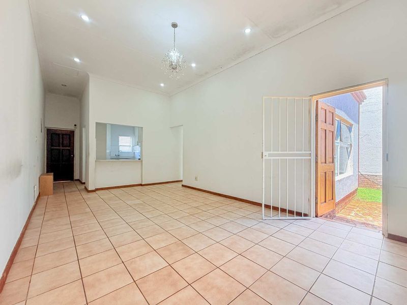 An open-plan living area featuring tiled flooring, recessed lighting, and a serving hatch connecting to the kitchen, with direct access to the exterior.