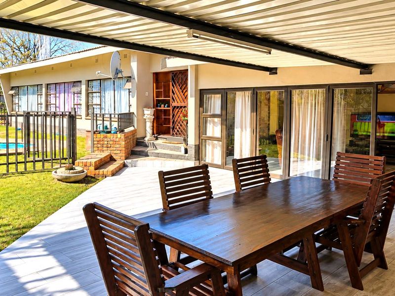 A spacious covered patio featuring tiled flooring and direct access to the garden and swimming pool area through large sliding glass doors.
