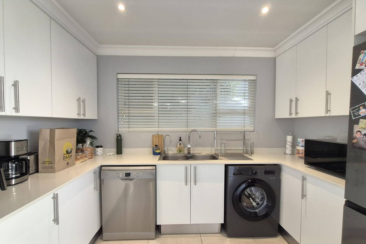 A modern, well-maintained kitchen featuring white cabinetry, stone countertops, a double sink, and integrated space for a dishwasher and washing machine.