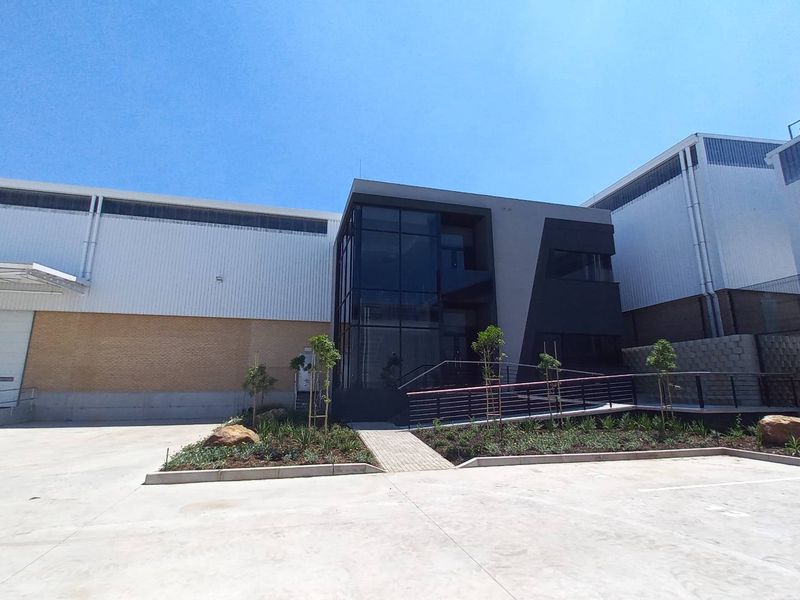Modern industrial facility featuring a glass-fronted office entrance, large roller shutter loading bay, and clean concrete yard area.