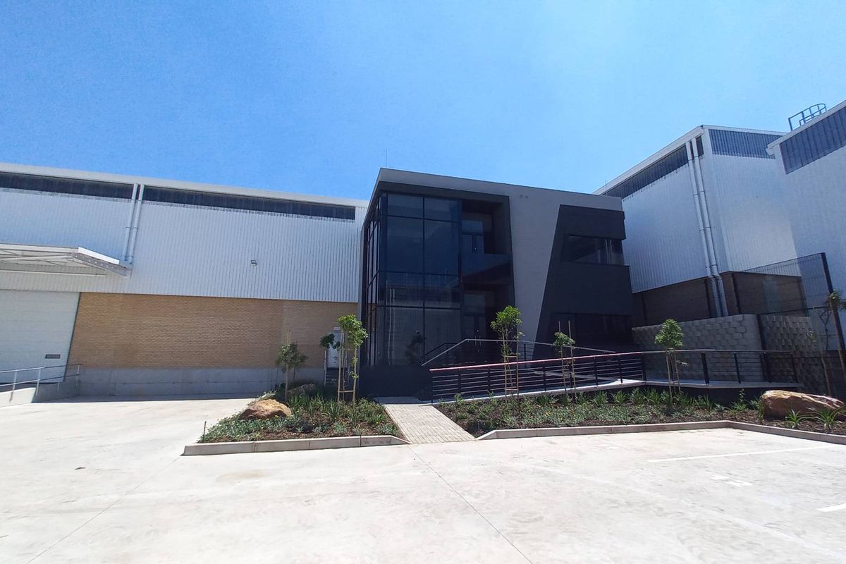 Modern industrial facility featuring a glass-fronted office entrance, large roller shutter loading bay, and clean concrete yard area.