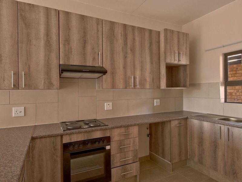A clean, modern kitchen featuring wood-look cabinetry, stone-effect countertops, built-in oven, electric hob, extractor fan, and a stainless steel double sink.