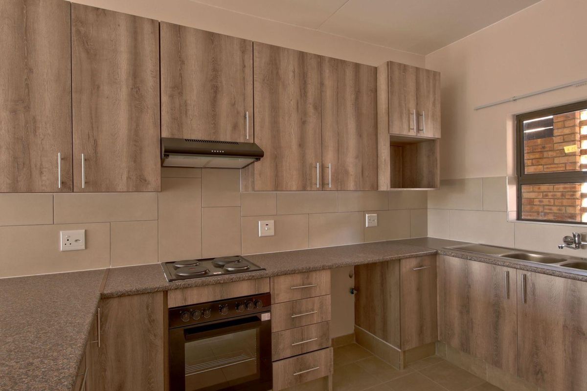 A clean, modern kitchen featuring wood-look cabinetry, stone-effect countertops, built-in oven, electric hob, extractor fan, and a stainless steel double sink.