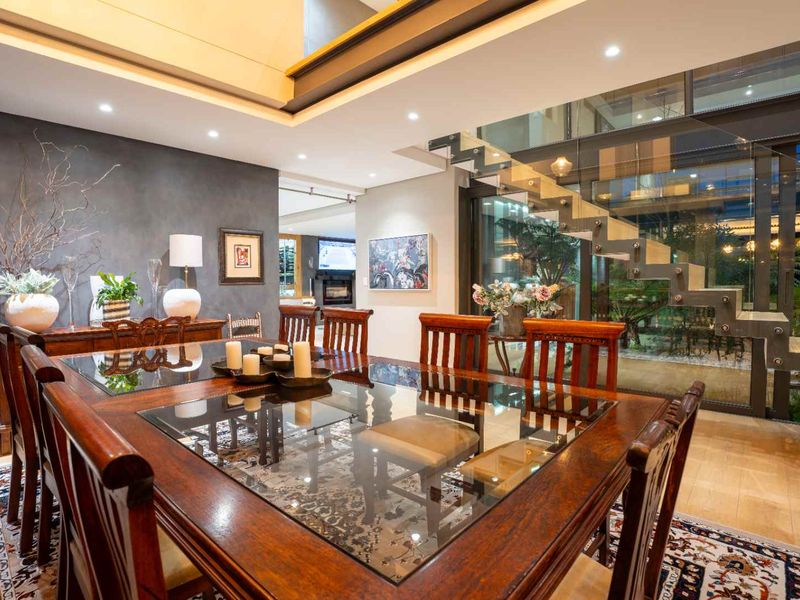 Elegant dining area featuring a modern floating staircase with glass balustrade, recessed lighting, and high-quality finishes in an open-plan layout.