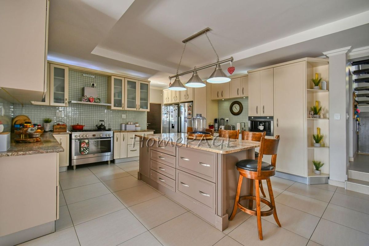 Spacious open-plan kitchen featuring a large central island, granite countertops, tiled flooring, and built-in cabinetry with integrated appliances.