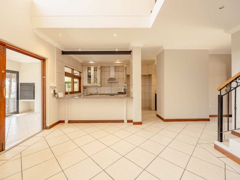 Spacious open-plan living area featuring tiled floors, a modern kitchen with granite countertops, and a staircase with wrought iron detailing.