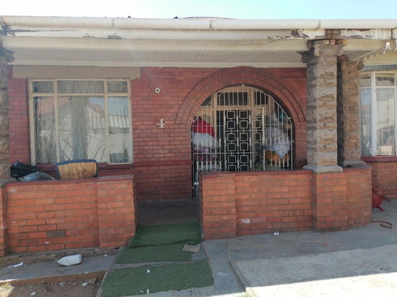 Front facade of a brick house featuring a covered porch, stone pillars, and security gate entrance.
