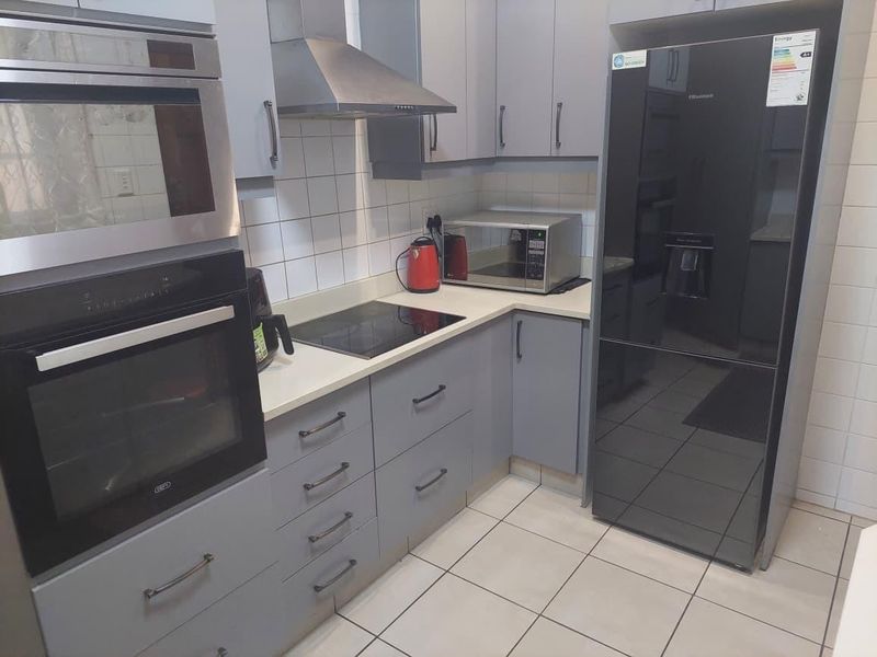 Modern kitchen featuring grey cabinetry, built-in oven, microwave, extractor fan, induction hob, and tiled flooring.