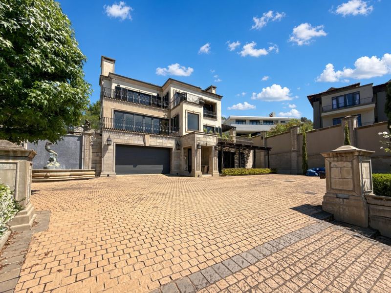 Impressive multi-story residence featuring a stone facade, paved driveway, double garage, and elegant wrought iron balcony railings with a decorative water feature.