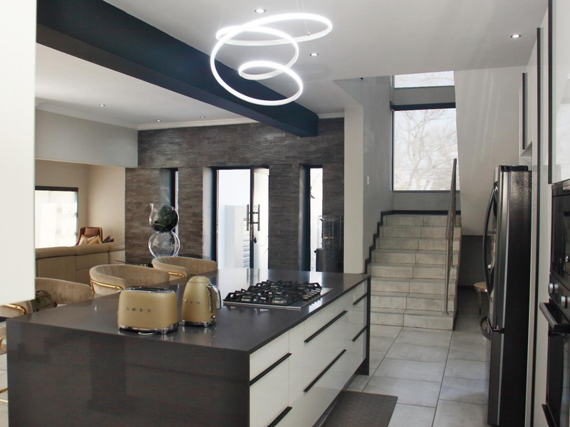 Modern open-plan kitchen and living area featuring a central island with gas cooktop, stone finishes, and a striking feature wall with staircase access.