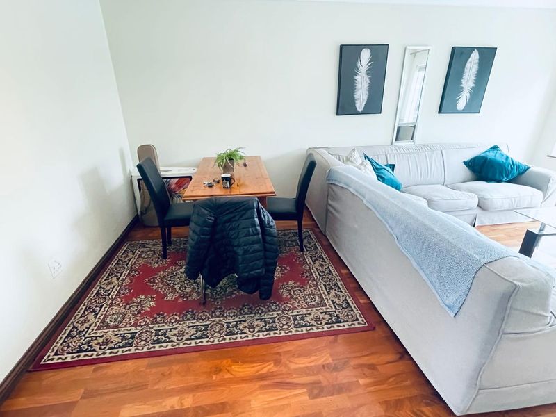 An open-plan living and dining area featuring warm-toned hardwood flooring and neutral wall finishes, providing a versatile space for relaxation and meals.