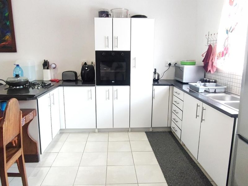 A functional kitchen featuring white cabinetry, dark countertops, a built-in oven, gas hob, and double sink with tiled flooring.